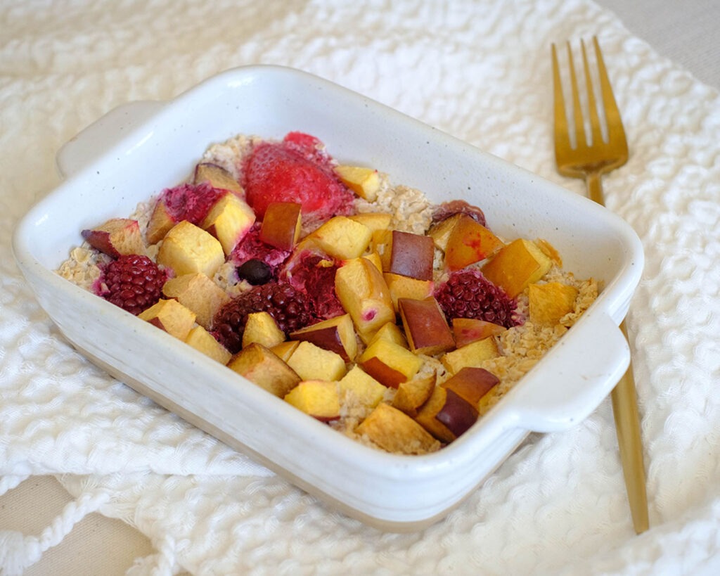Small baking dish holding baked oats topped with apricots and mixed berries.