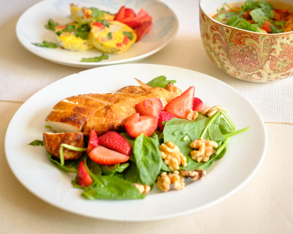 White round plate with baked balsamic chicken served with spinach, strawberries, and walnuts.