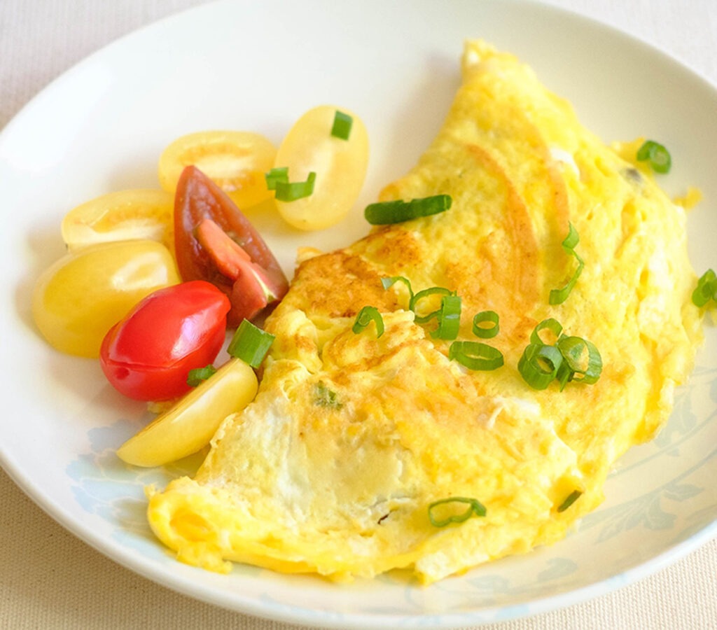 White round plate with an omelette garnished with fresh tomatoes and green onions.