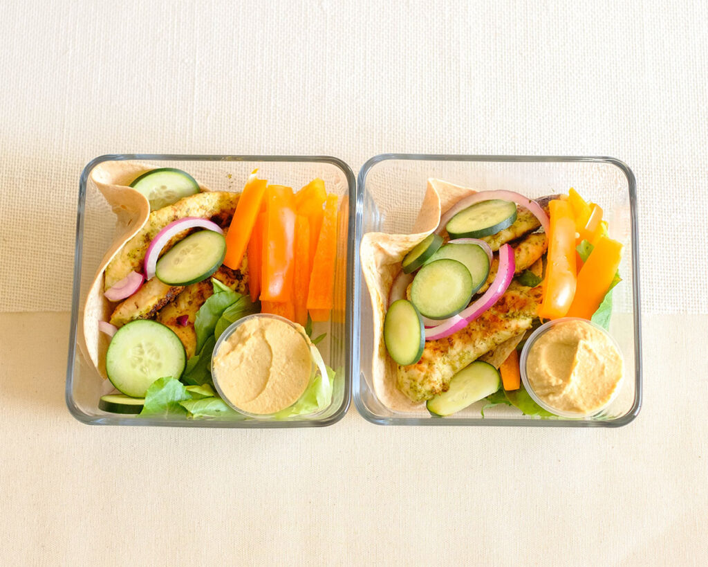 Glass meal prep containers with chicken pesto served with bell peppers and hummus dip.