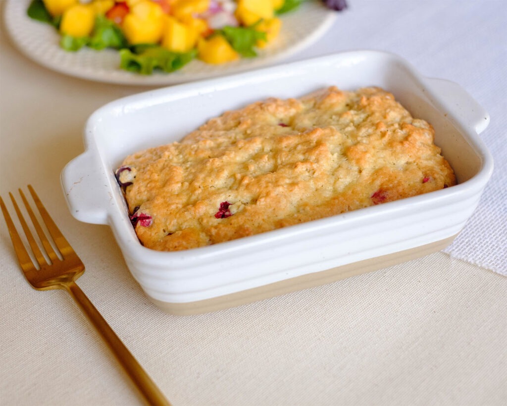 A small baking dish with a golden brown cranberry oatmeal muffin.
