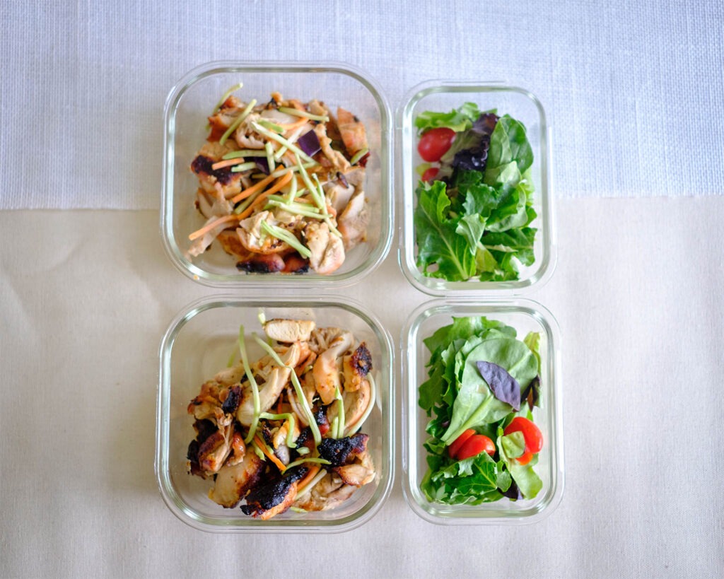 Baked honey mustard glazed chicken salad served with spring mix salad stored in a glass meal prep containers.