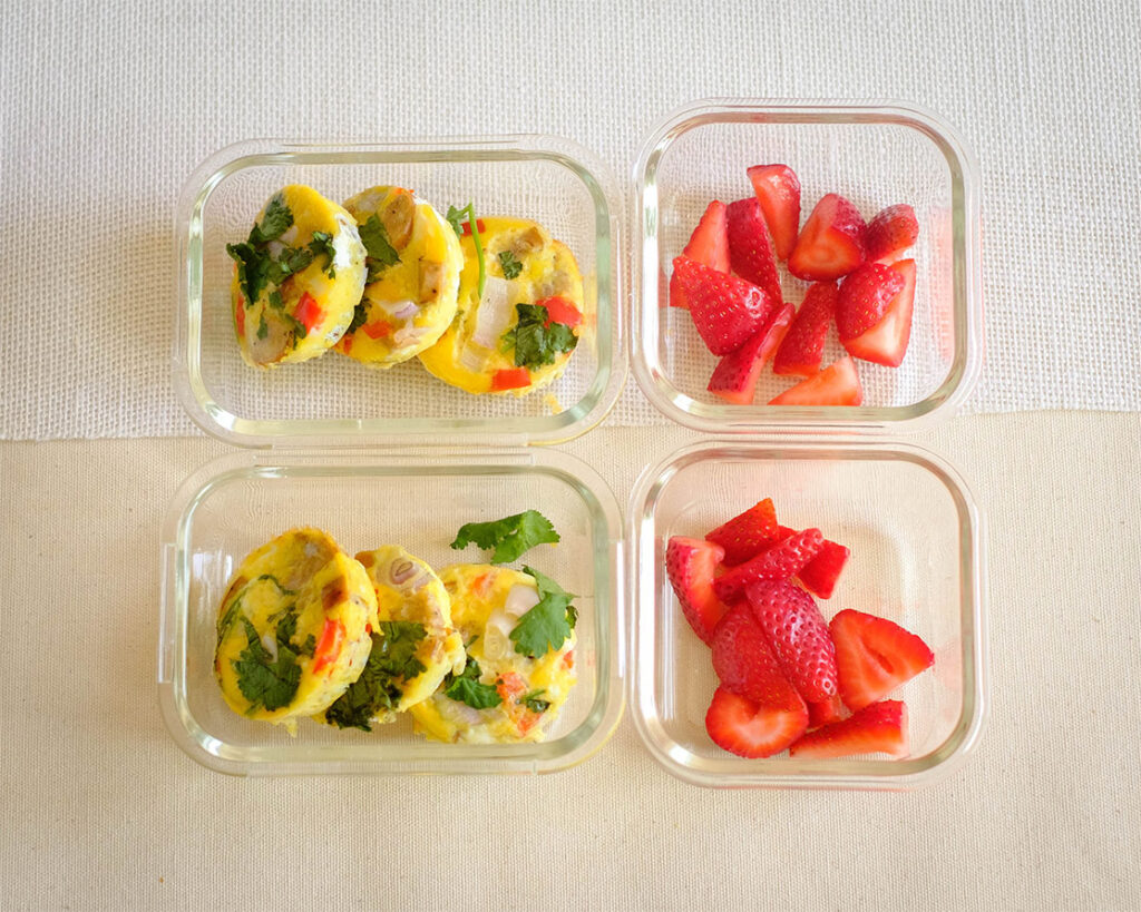 Glass meal prep containers storing sausage egg muffins and strawberries.