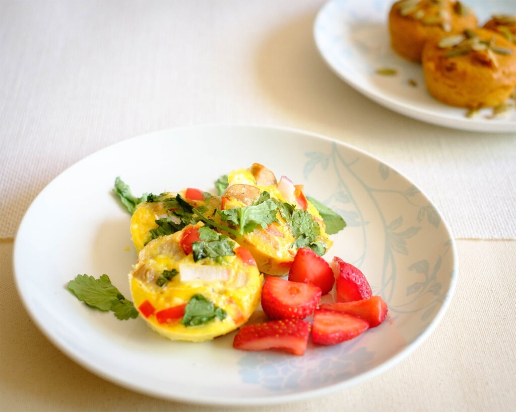 Round plate with breakfast sausage egg muffins served with strawberries and topped with fresh green herbs.