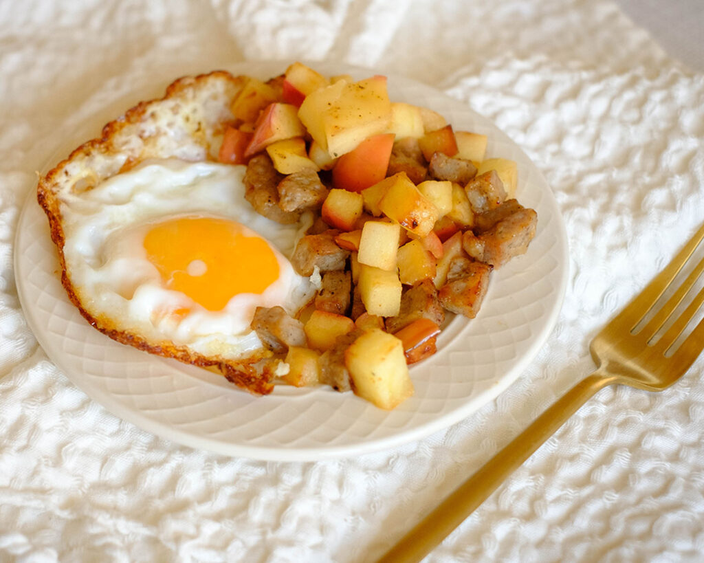 Plate with a crispy fried egg served with diced apples and chicken sausage.