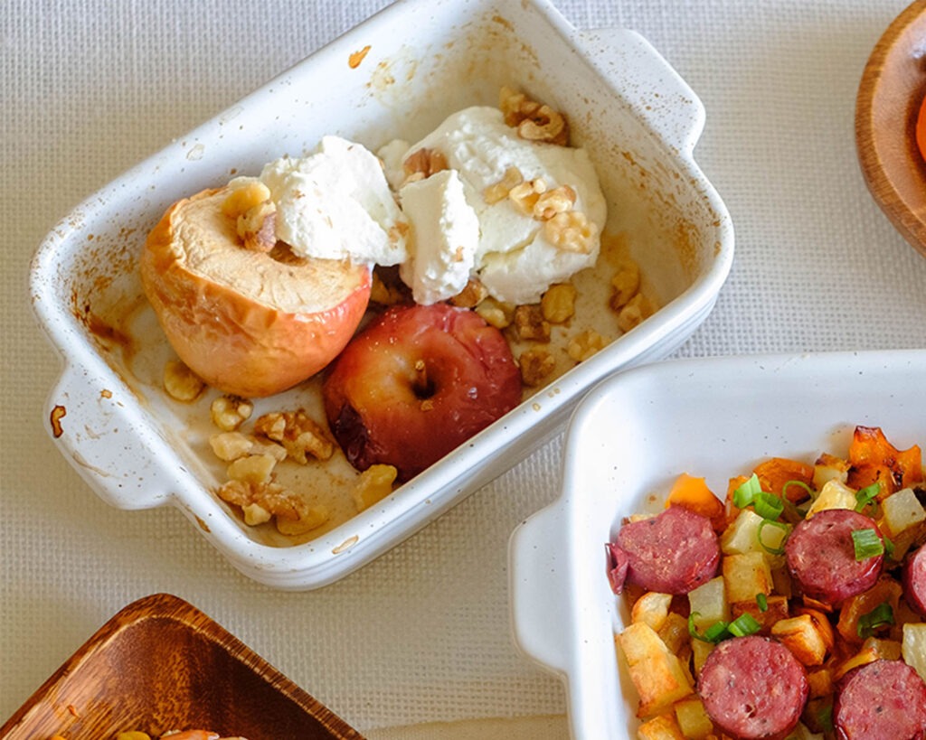 Small baking dish holding baked apples with ricotta cheese and walnuts.