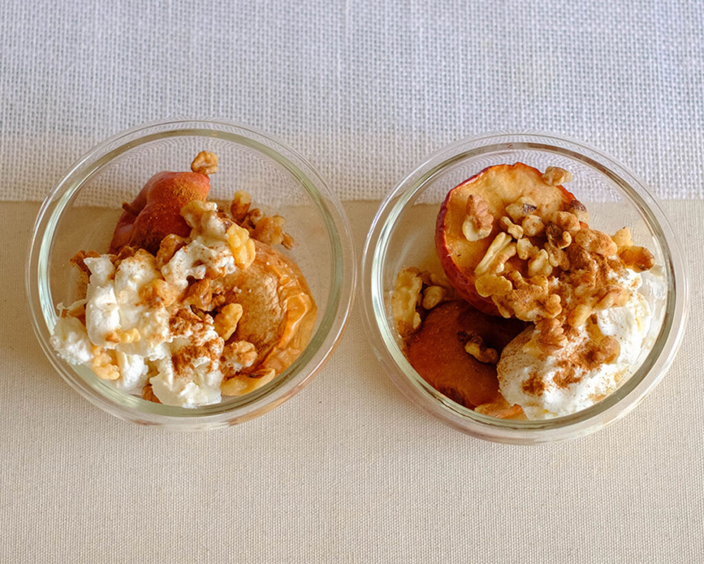 Glass meal prep containers holding baked apples with ricotta cheese and walnuts.