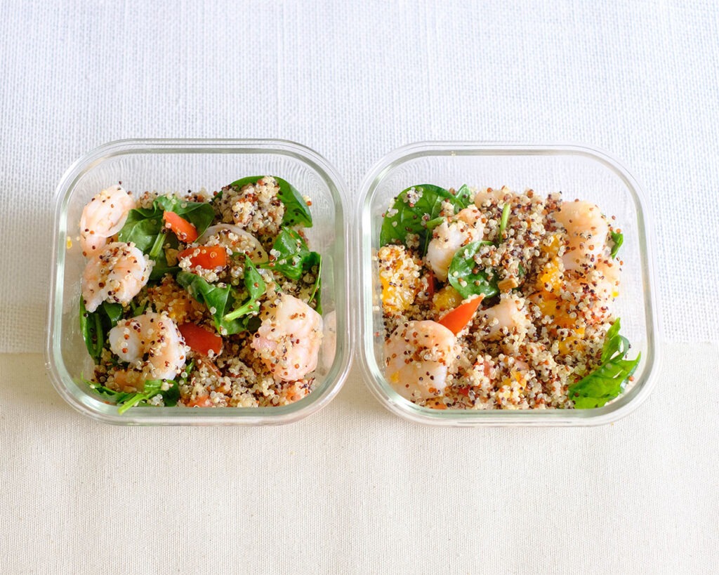 Glass meal prep containers with shrimp, quinoa, spinach, and mandarin oranges.