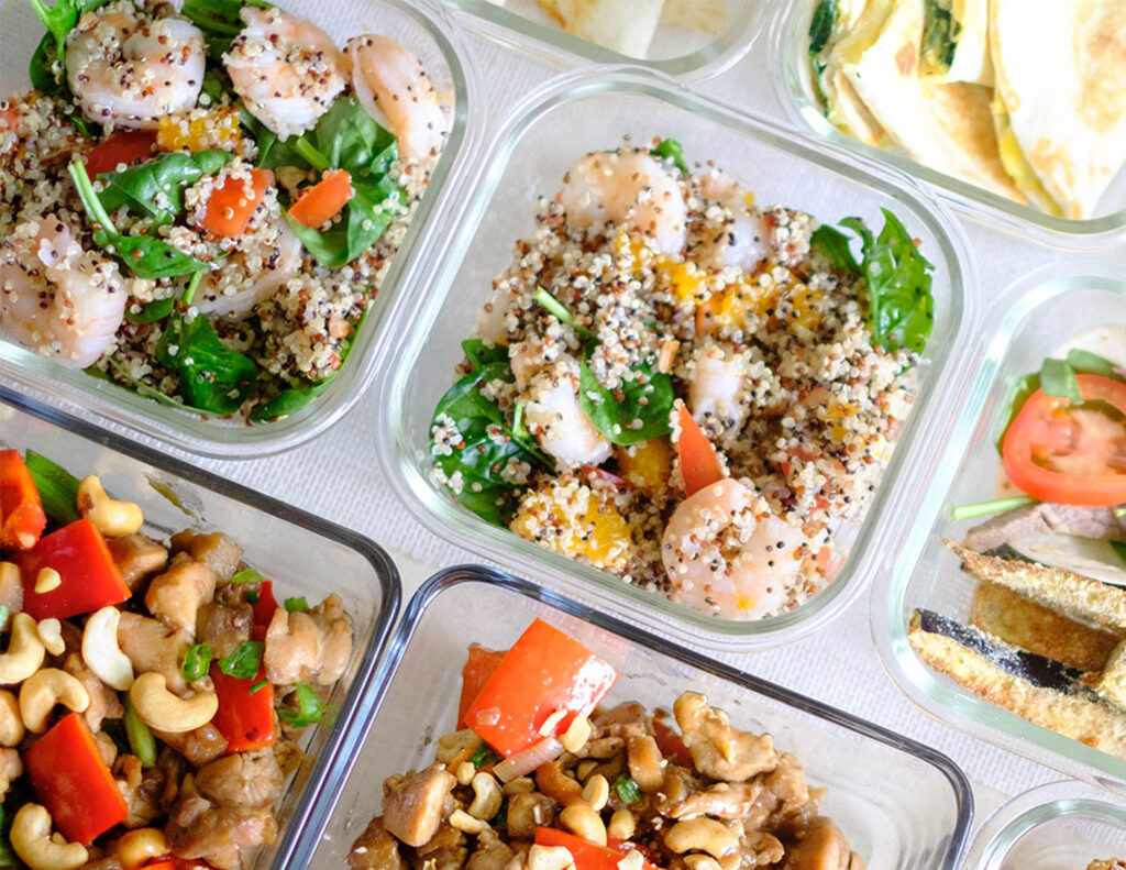 Glass meal prep containers with shrimp, quinoa, spinach, and mandarin oranges.