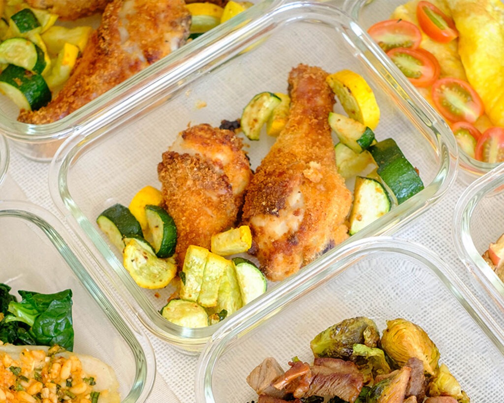 Glass meal prep container with crispy Air Fryer chicken with sliced yellow squash and zucchini.