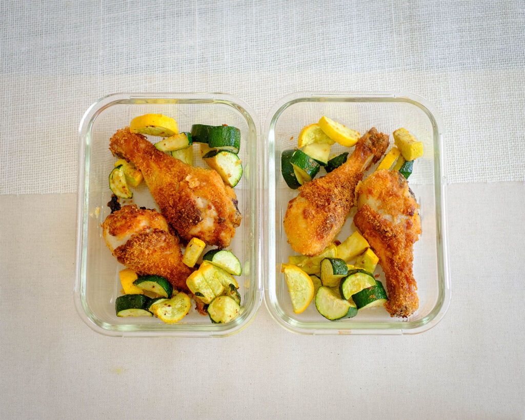 Glass meal prep containers with crispy Air Fryer chicken with sliced yellow squash and zucchini.