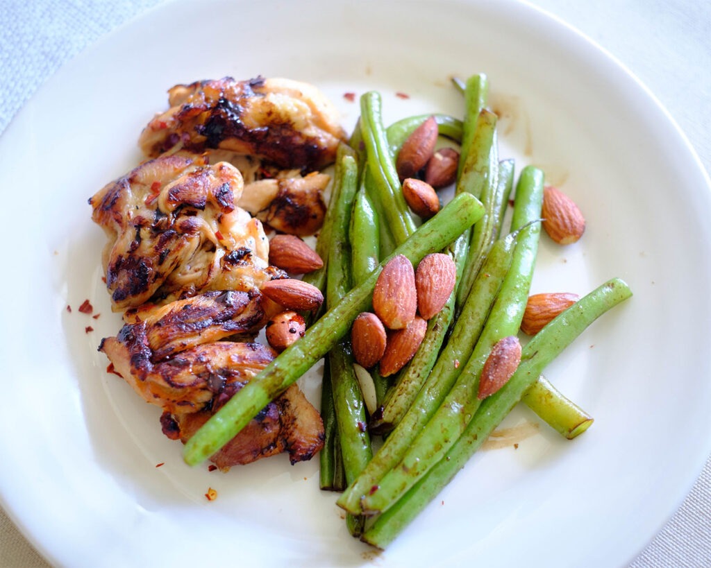 Round plate with grilled chicken and green beans with almonds.
