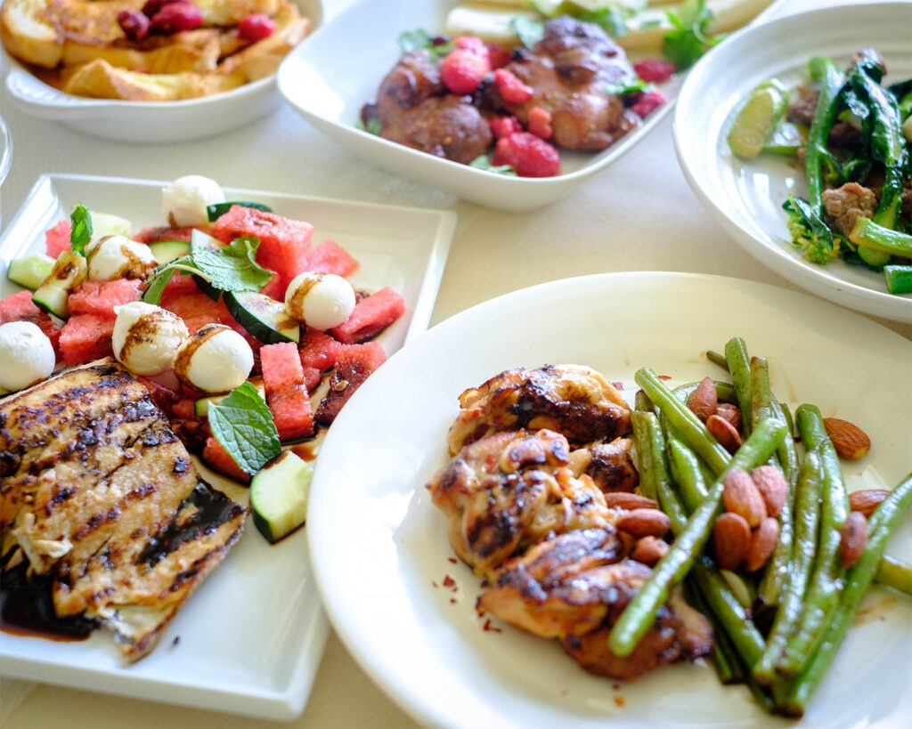 Several dishes including chicken with green beans and salmon with watermelon salad.