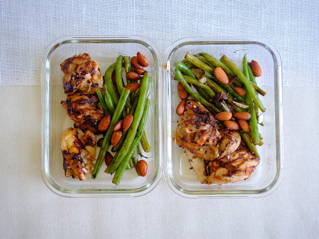 Glass meal prep containers storing grilled chicken, green beans, and almonds.