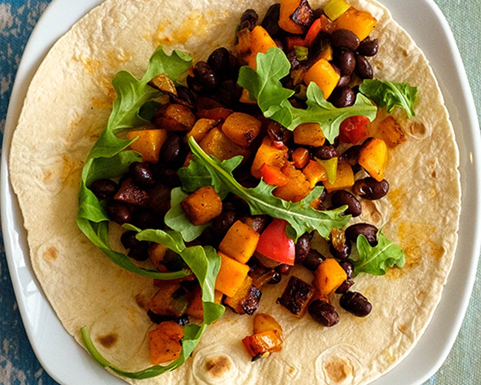 Plate with butternut squash and black bean taco topped with arugula.