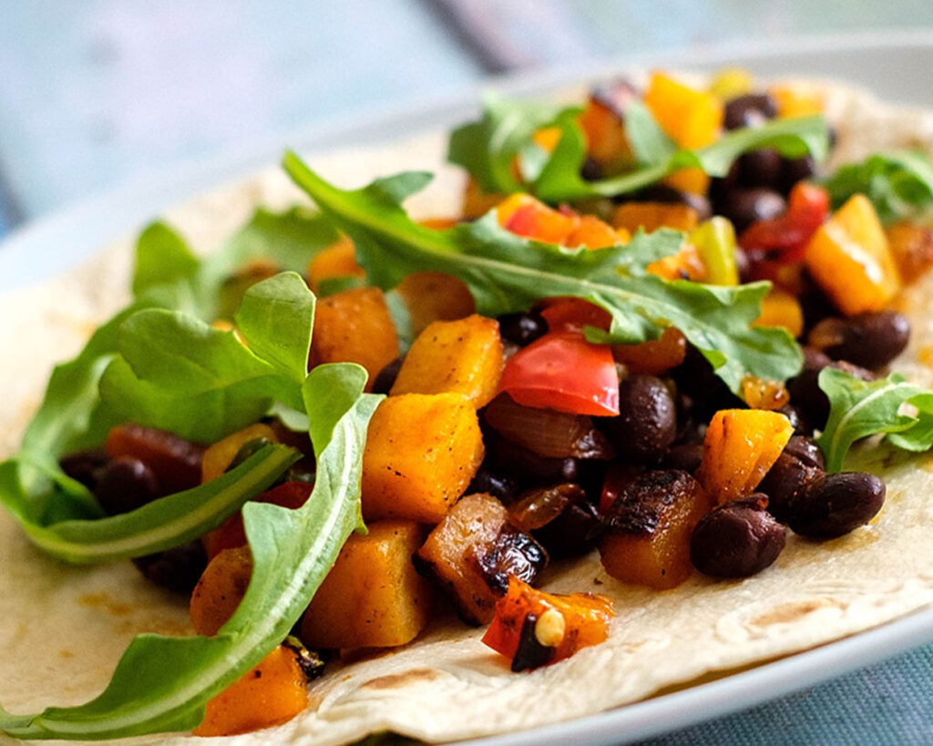 Plate with butternut squash and black bean taco topped with arugula.