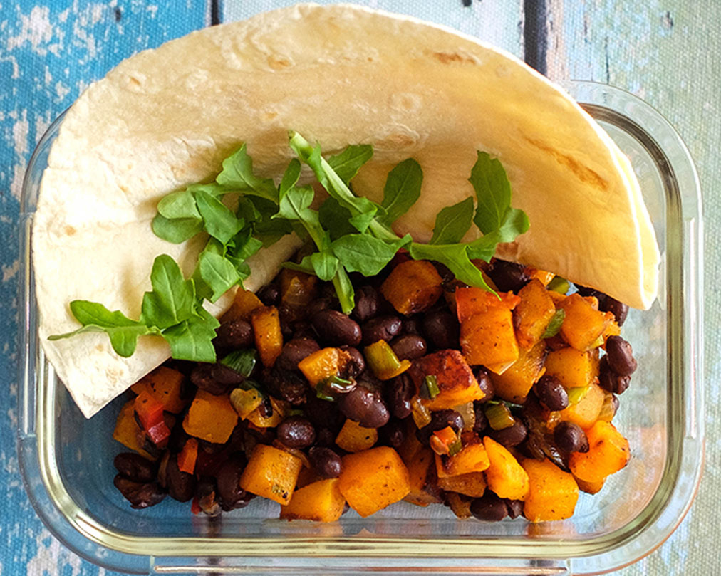 Glass meal prep container with butternut squash and black bean taco topped with arugula.