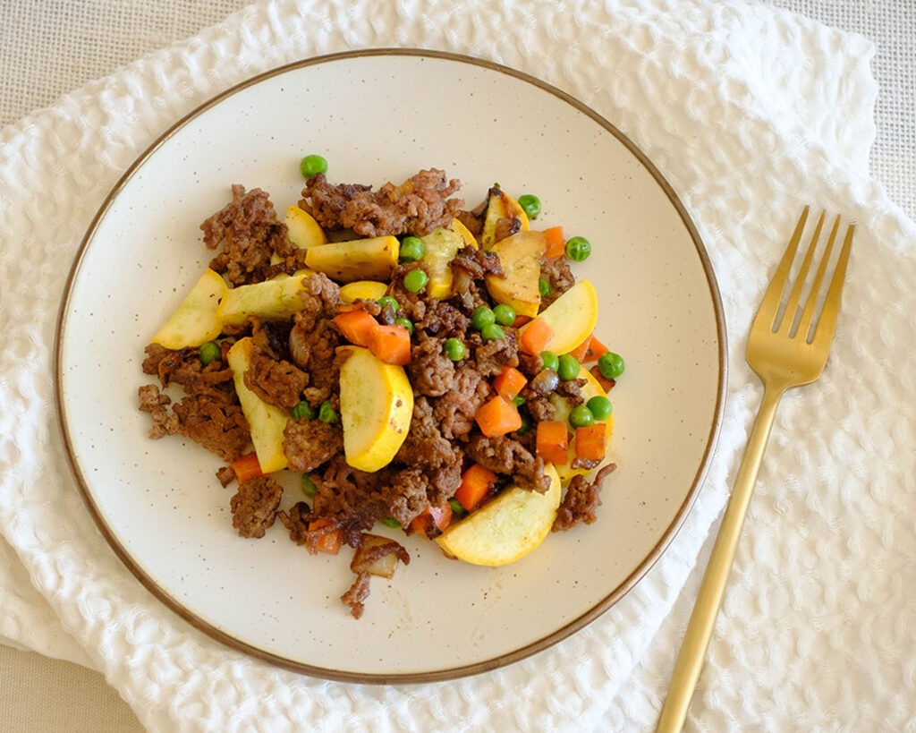Round plate with sauteed ground beef, yellow squash, peas, and carrots.