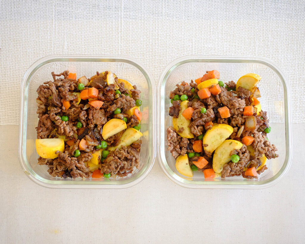 Glass meal prep containers with sauteed ground beef, yellow squash, peas, and carrots.