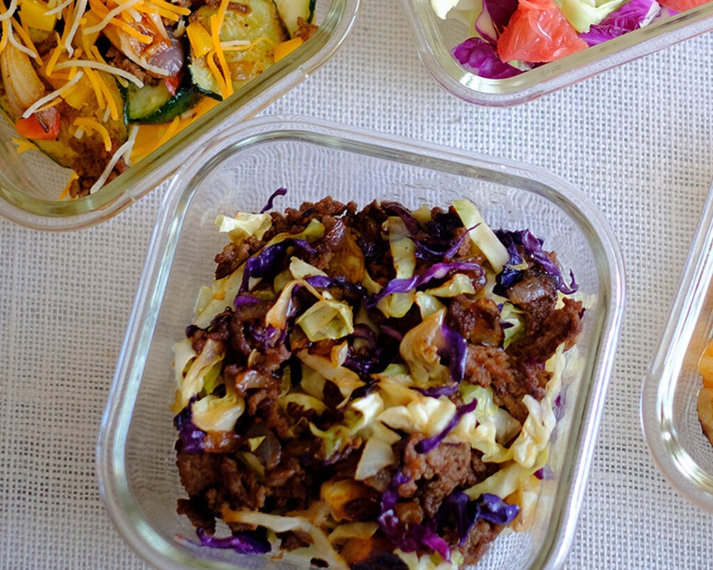 Glass meal prep container with stir fry ground beef with red and green shredded cabbage.