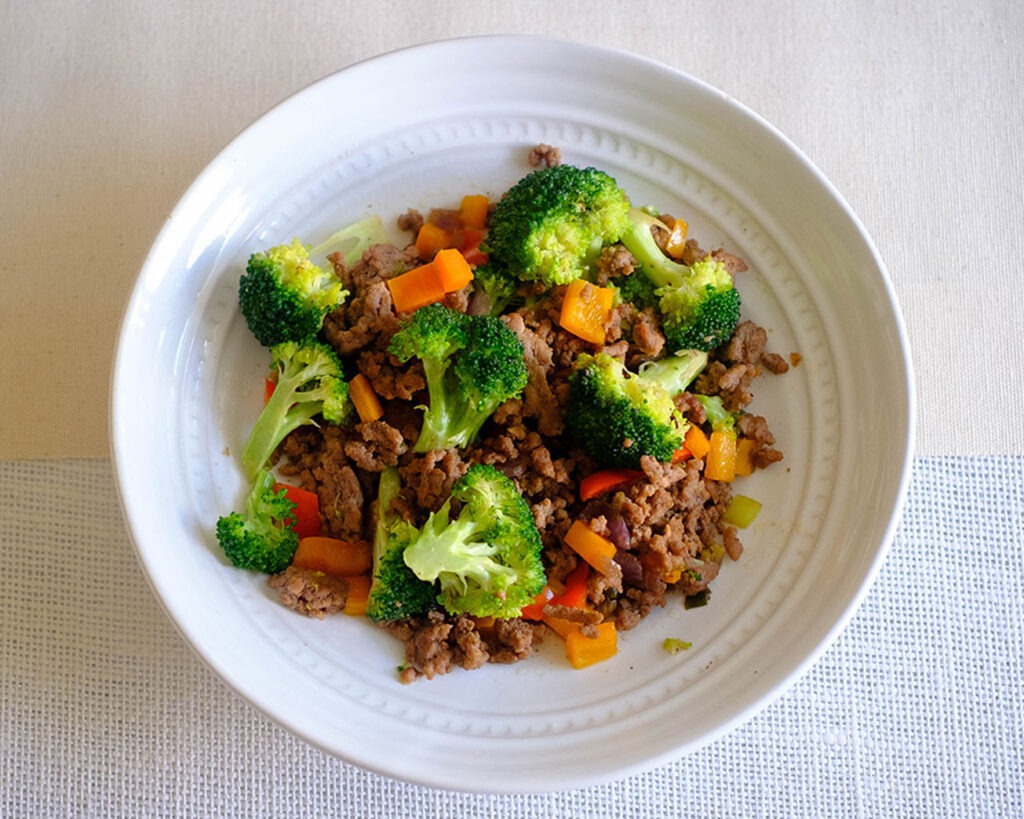 Round plate with stir fry ground beef with broccoli florets and diced red bell peppers.