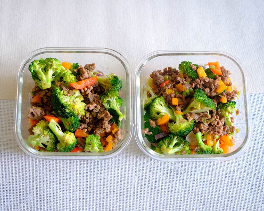 Glass meal prep containers with stir fry ground beef with broccoli florets and diced red bell peppers.