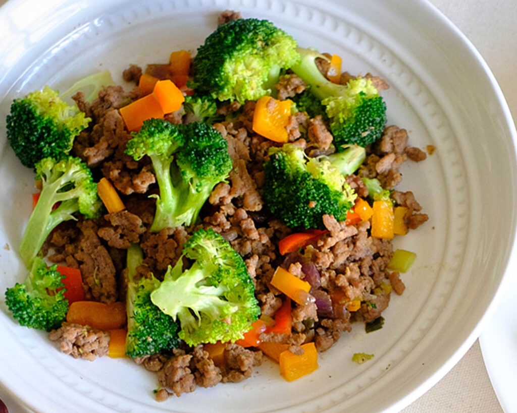 Round plate with stir fry ground beef with broccoli florets and diced red bell peppers.