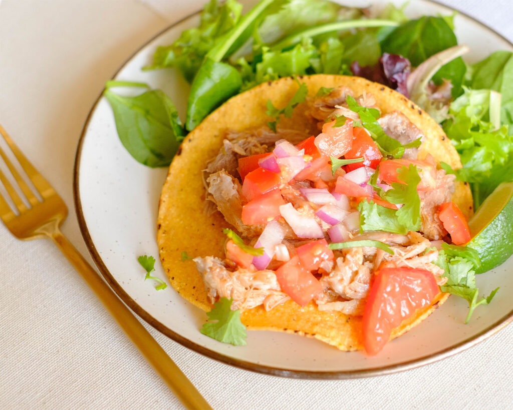 Plate with pork carnitas on tostada shells topped with fresh pico de gallo and served with a side salad.