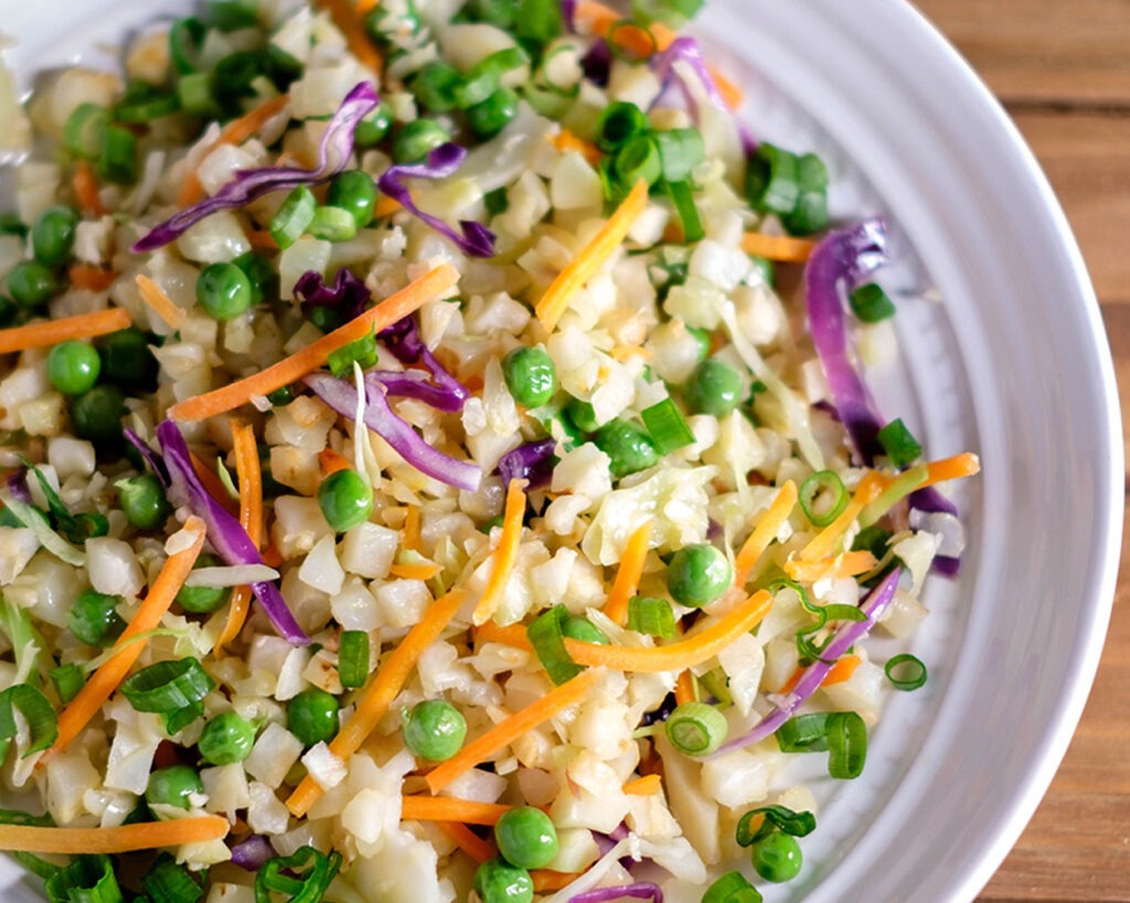 Round plate with a colorful cauliflower fried rice with peas, carrots, and shredded cabbage.