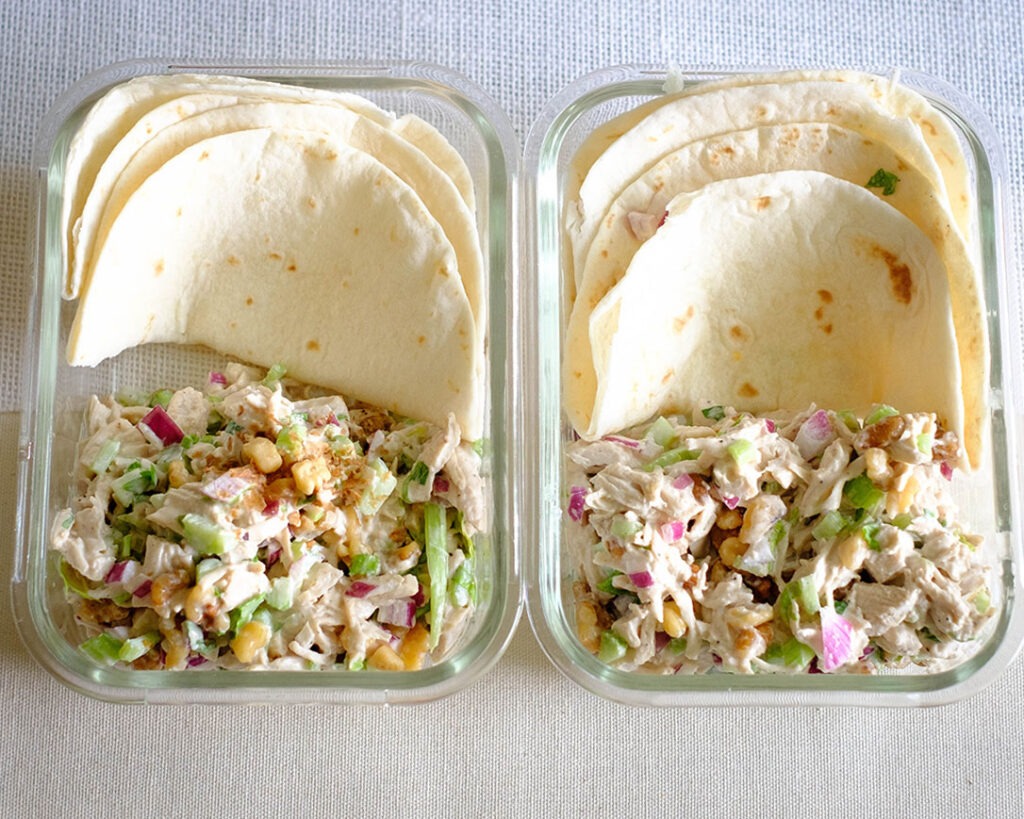 Glass meal prep containers storing celery chicken salad served in tortilla wraps.