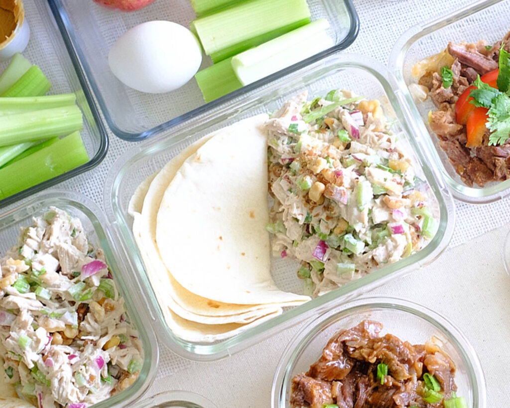 Glass meal prep containers storing celery chicken salad served in tortilla wraps.