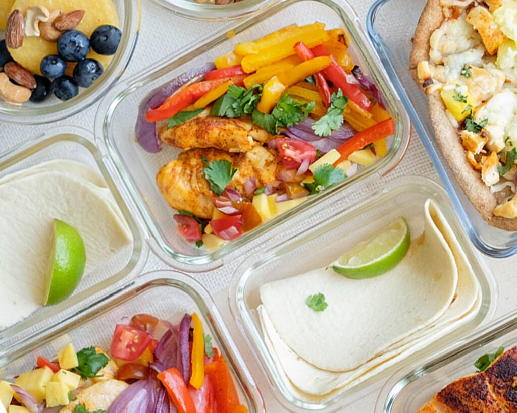 Glass meal prep container with chicken fajitas, mango salsa, and colorful bell peppers and onions served with tortillas.