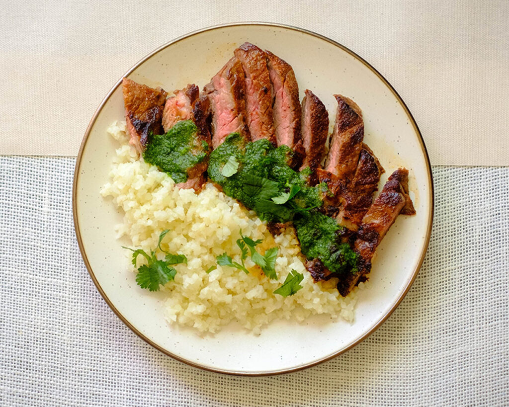 Round plate with grilled steak with cilantro pesto and cauliflower rice.