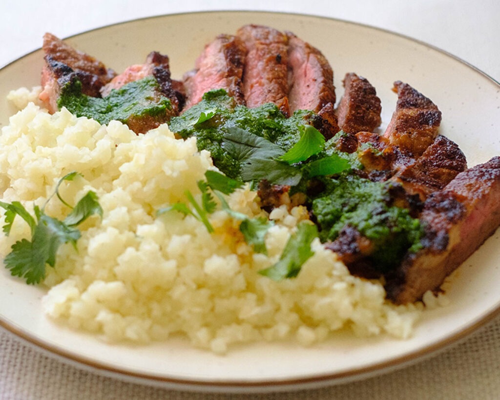 Round plate with grilled steak with cilantro pesto and cauliflower rice.