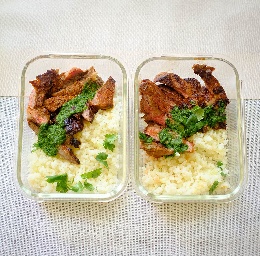 Glass meal prep containers with grilled steak with cilantro pesto and cauliflower rice.