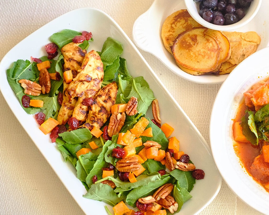 Plate with chicken served on top of baby kale salad with sweet potato, cranberries, and pecans.