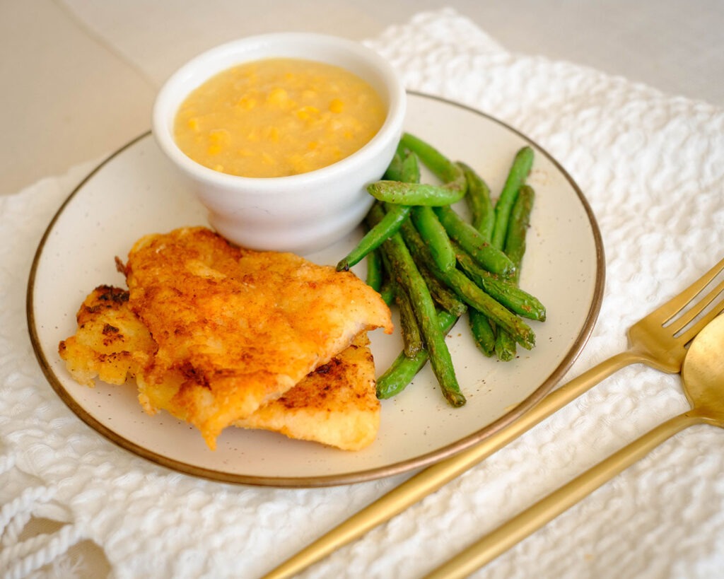 Round plate with pan-fried fish, green beans, and creamed corn - healthy fish and chips on a plate