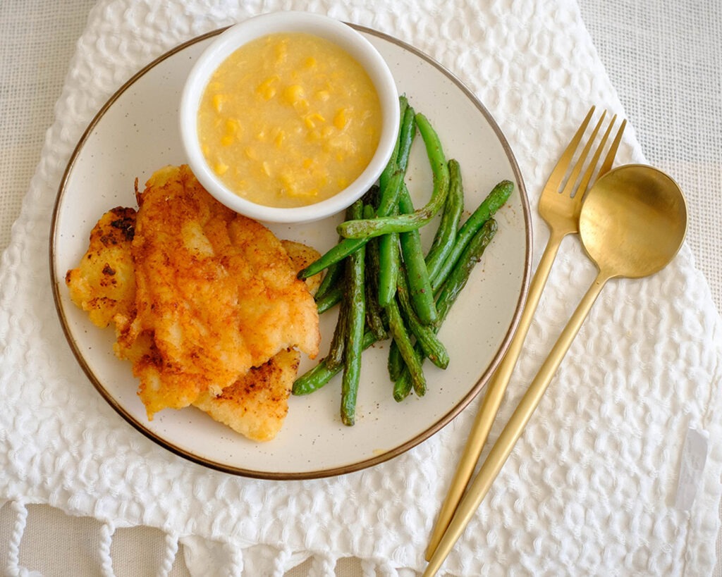 Round plate with pan-fried fish, green beans, and creamed corn - healthy fish and chips on a plate.