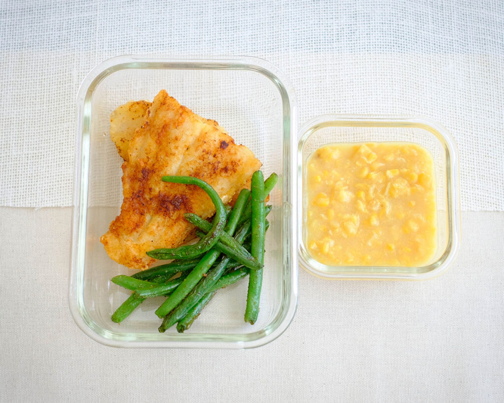 Glass meal prep containers with pan-fried fish, green beans, and creamed corn - healthy fish and chips.