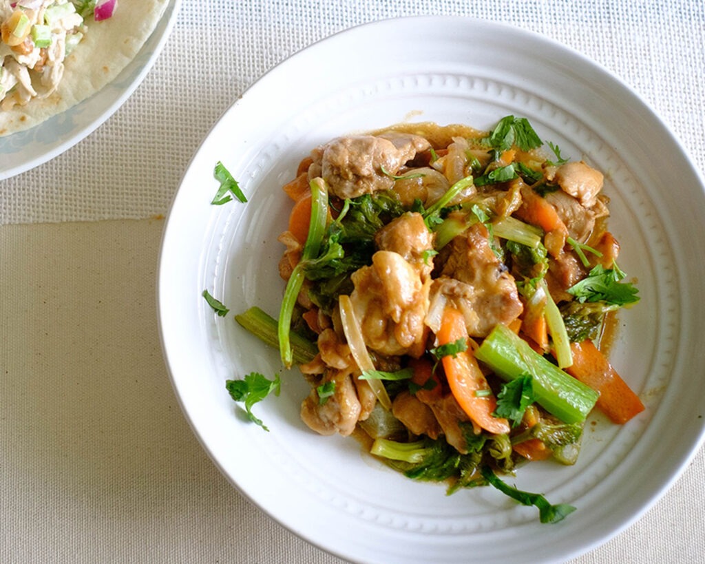 Round plate with stir fry chicken, celery, and carrots in a peanut sauce.