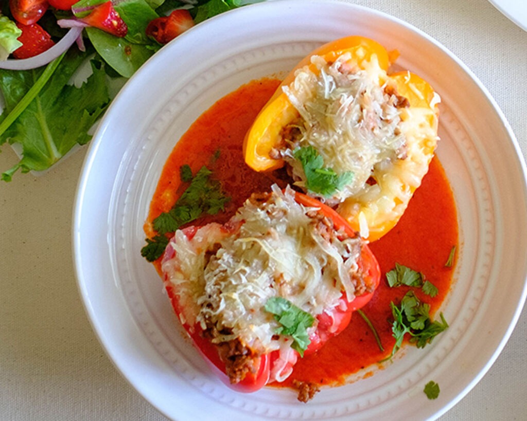 Round plate with bell peppers stuffed with meat sauce and topped with melted cheese.