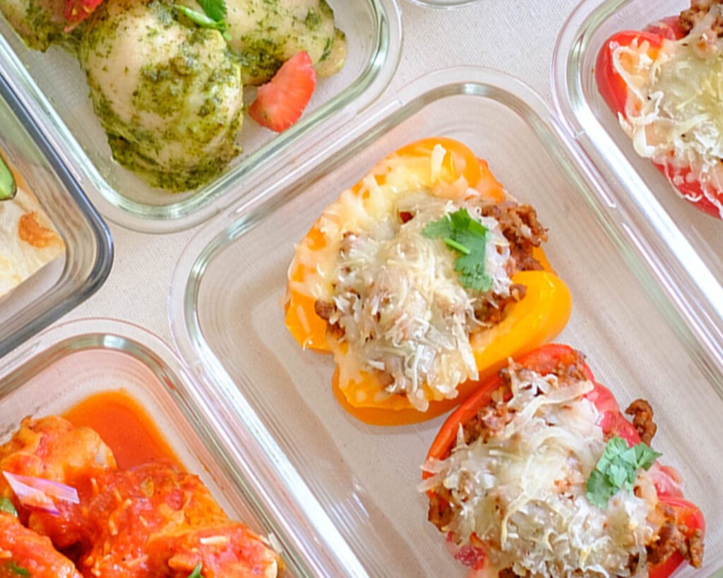 Glass meal prep containers with bell peppers stuffed with meat sauce and topped with melted cheese.