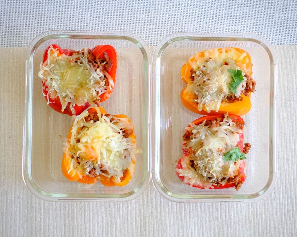Glass meal prep containers with bell peppers stuffed with meat sauce and topped with melted cheese.