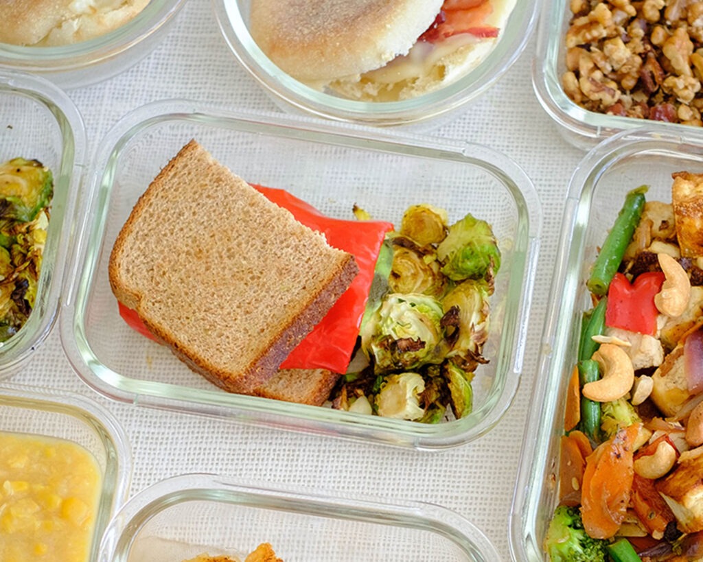 Glass meal prep container with a grilled cheese and vegetable sandwich with roasted brussels sprouts.