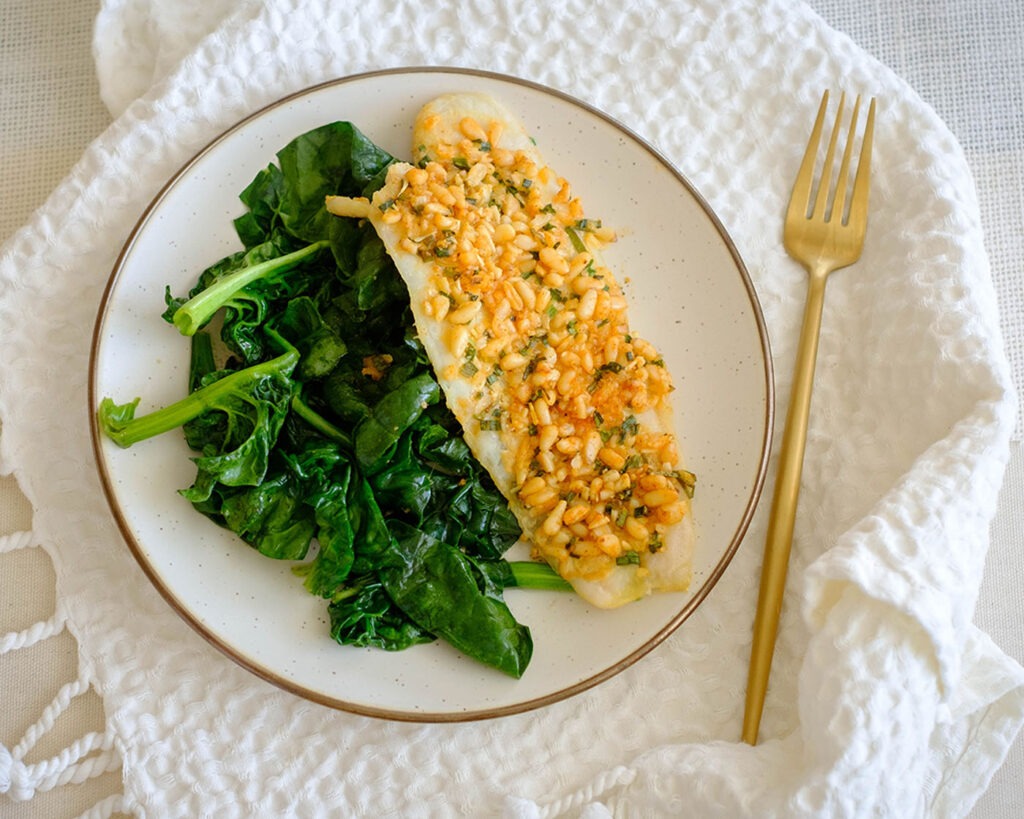 Round plate with baked pine nut crusted tilapia with sauteed spinach.