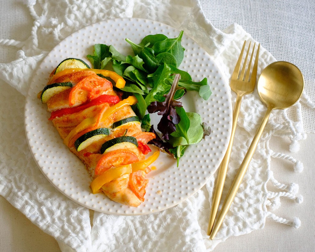 Round plate with baked chicken breasts stuffed with colorful vegetables and a side salad.