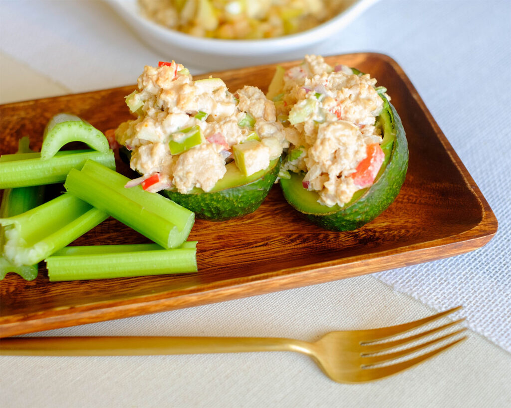Wood plate with avocado stuffed with salmon salad and celery sticks.
