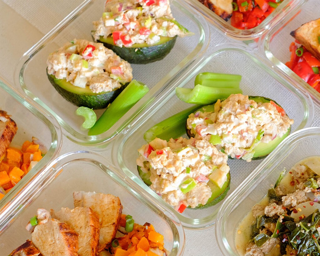 Glass meal prep containers with avocado stuffed with salmon salad and celery sticks.