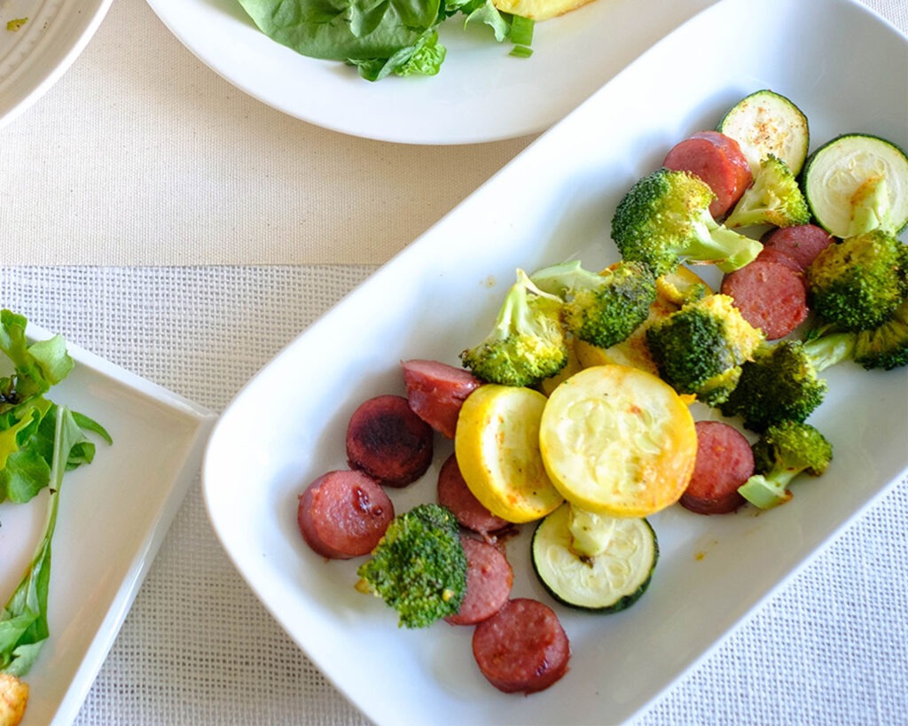 Plate with roasted sausage, zucchini, yellow squash, and broccoli florets.
