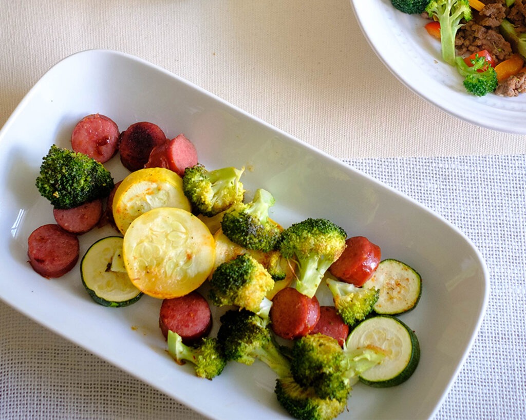 Plate with roasted sausage, zucchini, yellow squash, and broccoli florets.